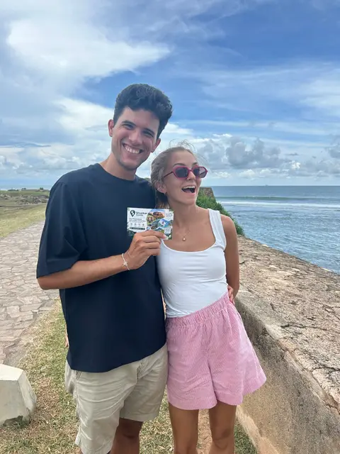 Two travellers by the sea at Galle Fort holding a Srilankan Guide card